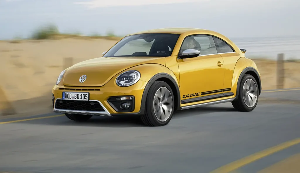 VW Beetle Dune in Sandstorm Yellow Metallic driving on a beach road.