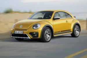 VW Beetle Dune in Sandstorm Yellow Metallic driving on a beach road.