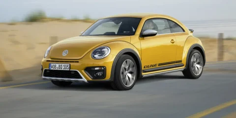 VW Beetle Dune in Sandstorm Yellow Metallic driving on a beach road.