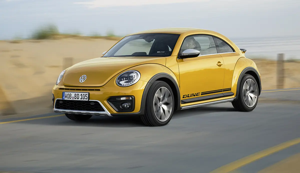 VW Beetle Dune in Sandstorm Yellow Metallic driving on a beach road.