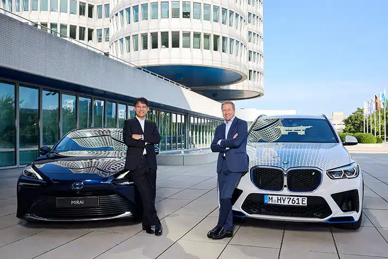 BMW Chairman Oliver Zipse and Toyota President Koji Sato announce fuel cell collaboration on September 5, 2024, standing beside BMW and Toyota vehicles.