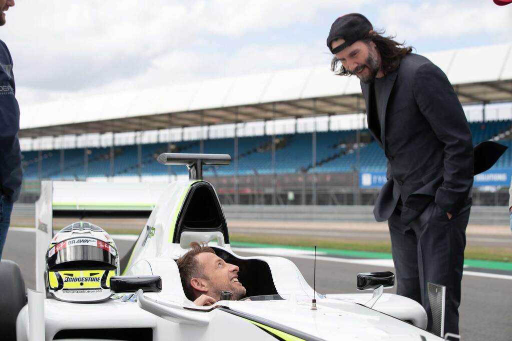 Keanu Reeves talking to F1's Jenson Button on a race track