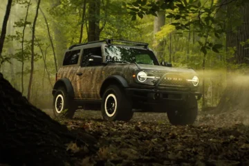 Bronco Sasquatch Searcher SUV camouflaged in dense forest off-road terrain.