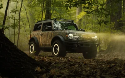 Bronco Sasquatch Searcher SUV camouflaged in dense forest off-road terrain.