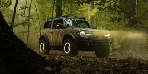 Bronco Sasquatch Searcher SUV camouflaged in dense forest off-road terrain.