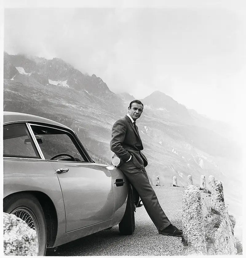 Sean Connery as Bond leaning against the original Aston Martin DB5 during Goldfinger filming on Furka Pass.