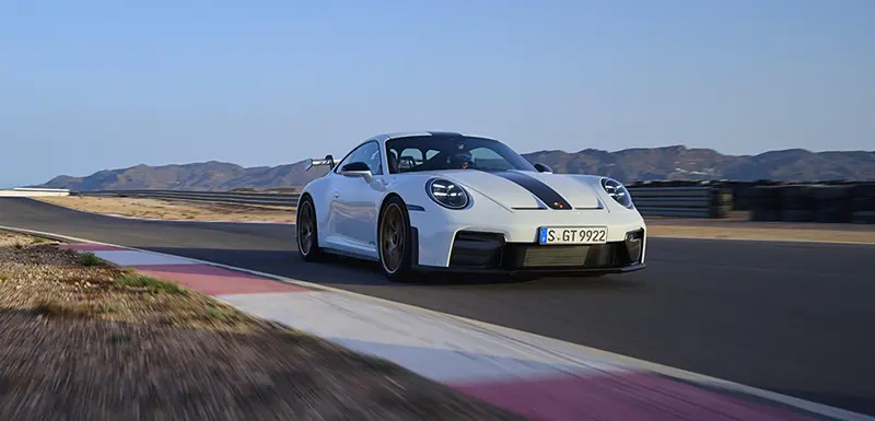 A white 2024 Porsche 911 GT Weissach Package showcasing its looks and power on a racetrack.