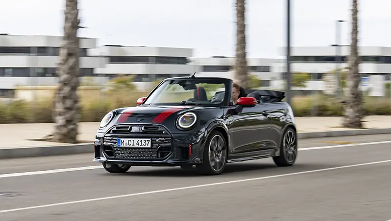 Mini John Cooper Works Cabriolet driving with the roof down, showcasing its sporty and open-air design.