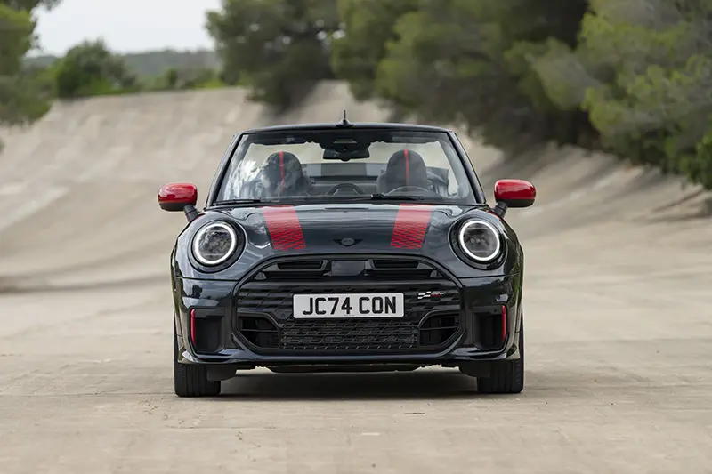 Front view of the new Mini John Cooper Works Cabriolet with the roof down, showcasing its bold grille and headlights.