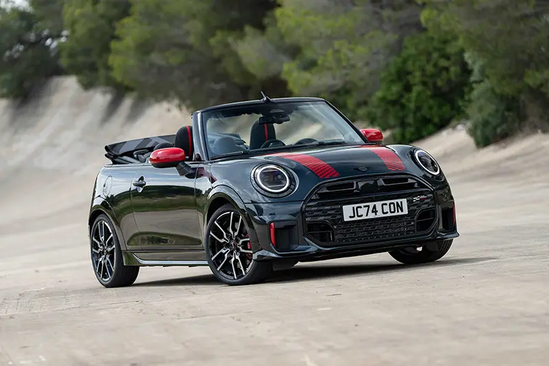 Front 3/4 profile of the Mini JCW Cabriolet with its roof down, showcasing bold styling.