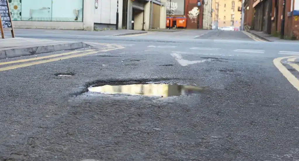Large water-filled pothole in the middle of a busy London city street