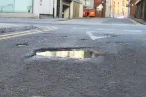 Large water-filled pothole in the middle of a busy London city street