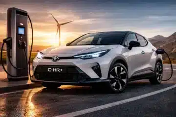 Toyota C-HR+ all-electric SUV charging at a rapid charger with wind turbine in the background at sunset