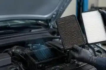 Mechanic comparing a clogged engine air filter with a clean replacement beside an open car engine air filter housing