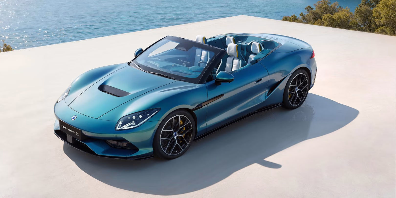 Teal BYD Denza Z Spider convertible, roof down, high front three-quarter view beside the sea