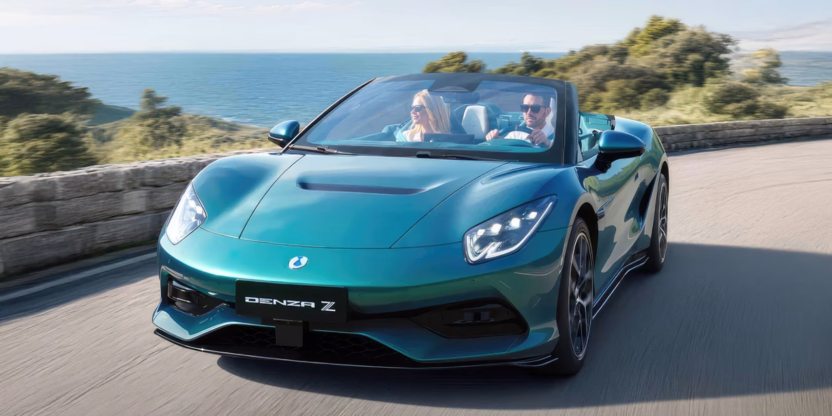 Teal BYD Denza Z Spider driving on a coastal road with two occupants, roof down