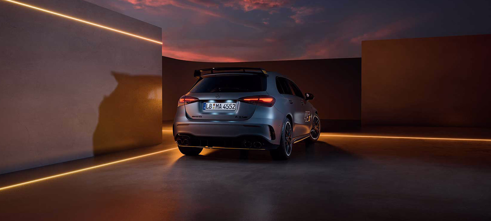 Grey Mercedes-AMG A45 S Final Edition from the rear showing its roof spoiler and quad tailpipes, in a dusk studio setting