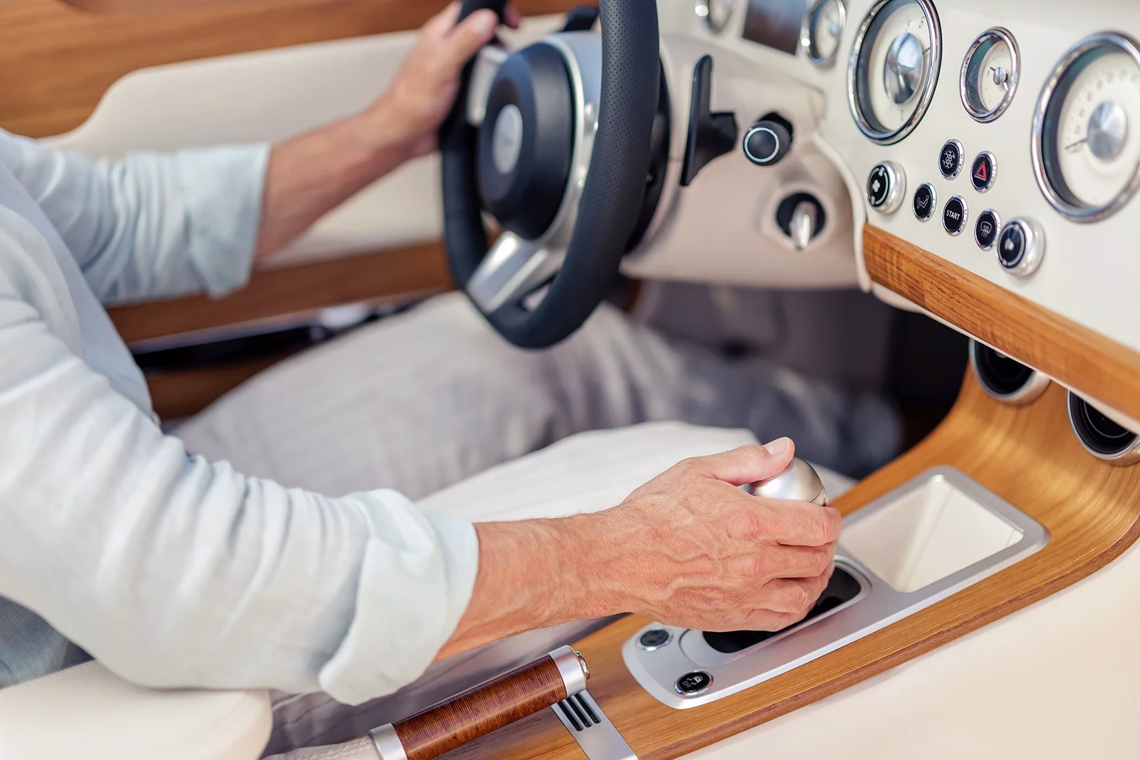 Driver's hand on the metal gearshift of the Morgan Midsummer Coupé, beside a wood console and chrome-ringed dials