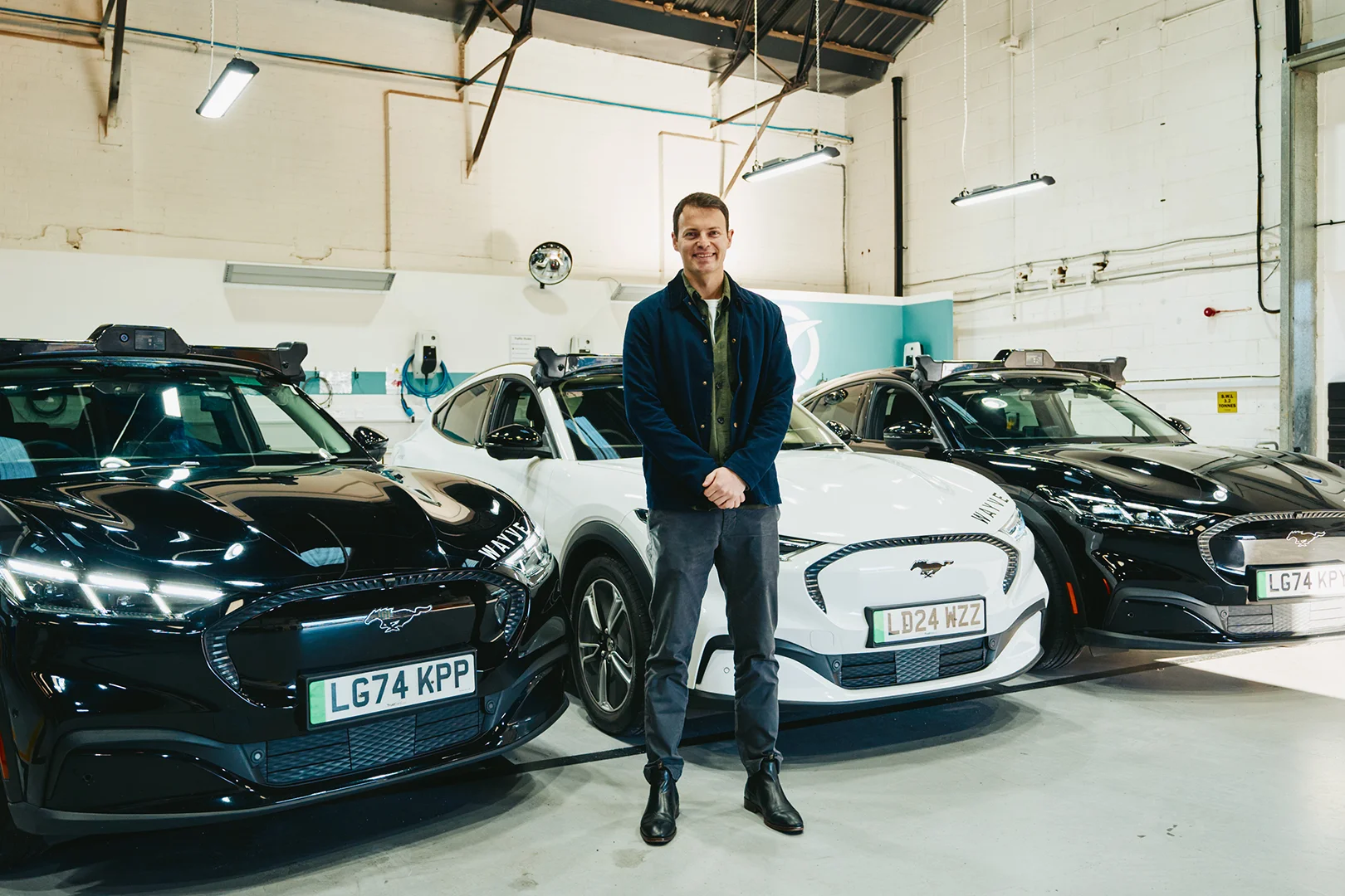 Alex Kendall next to a series of Wayve new, driverless cars