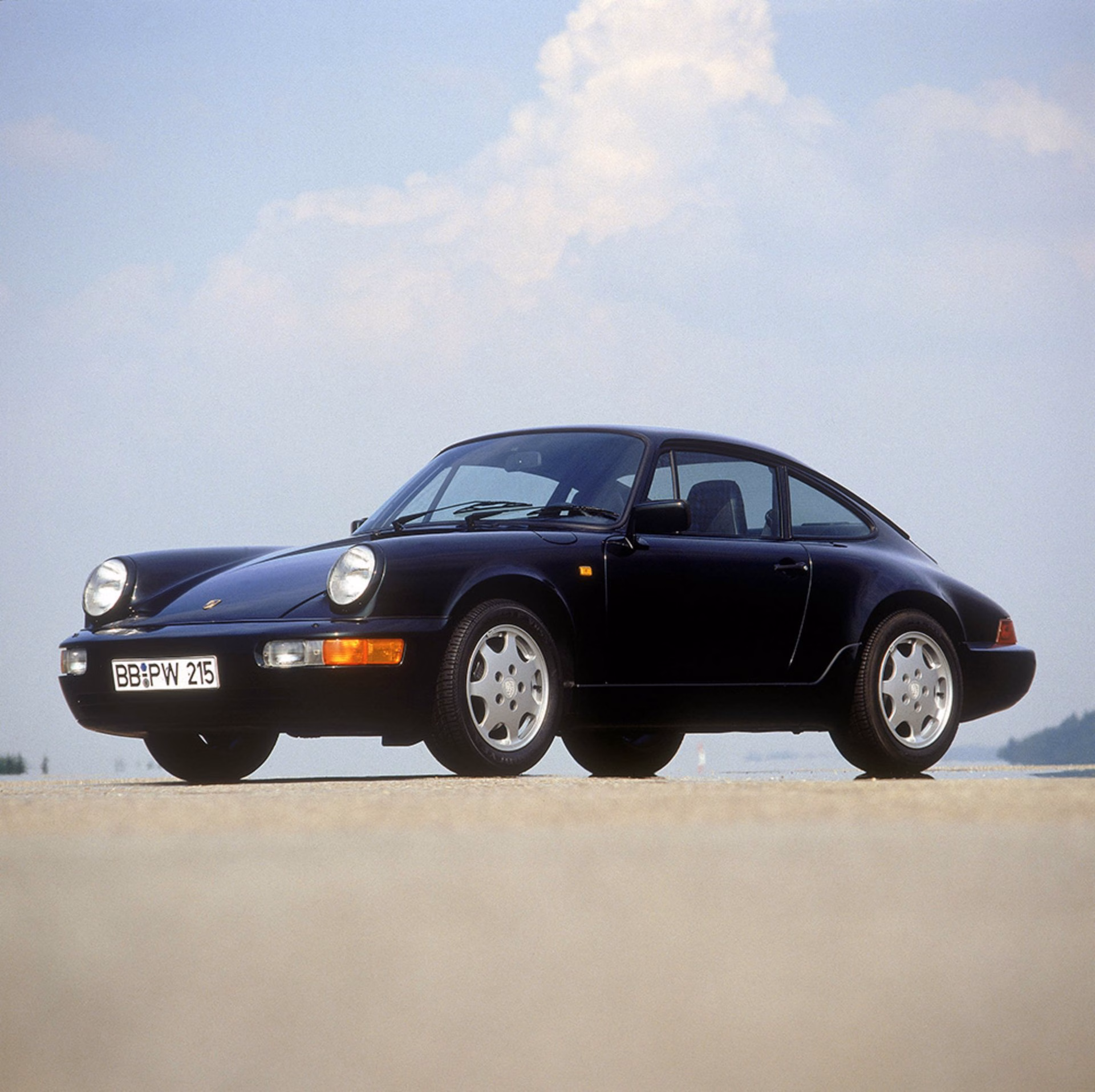 Black Porsche 911 964 Carrera front three quarter view against a bright sky