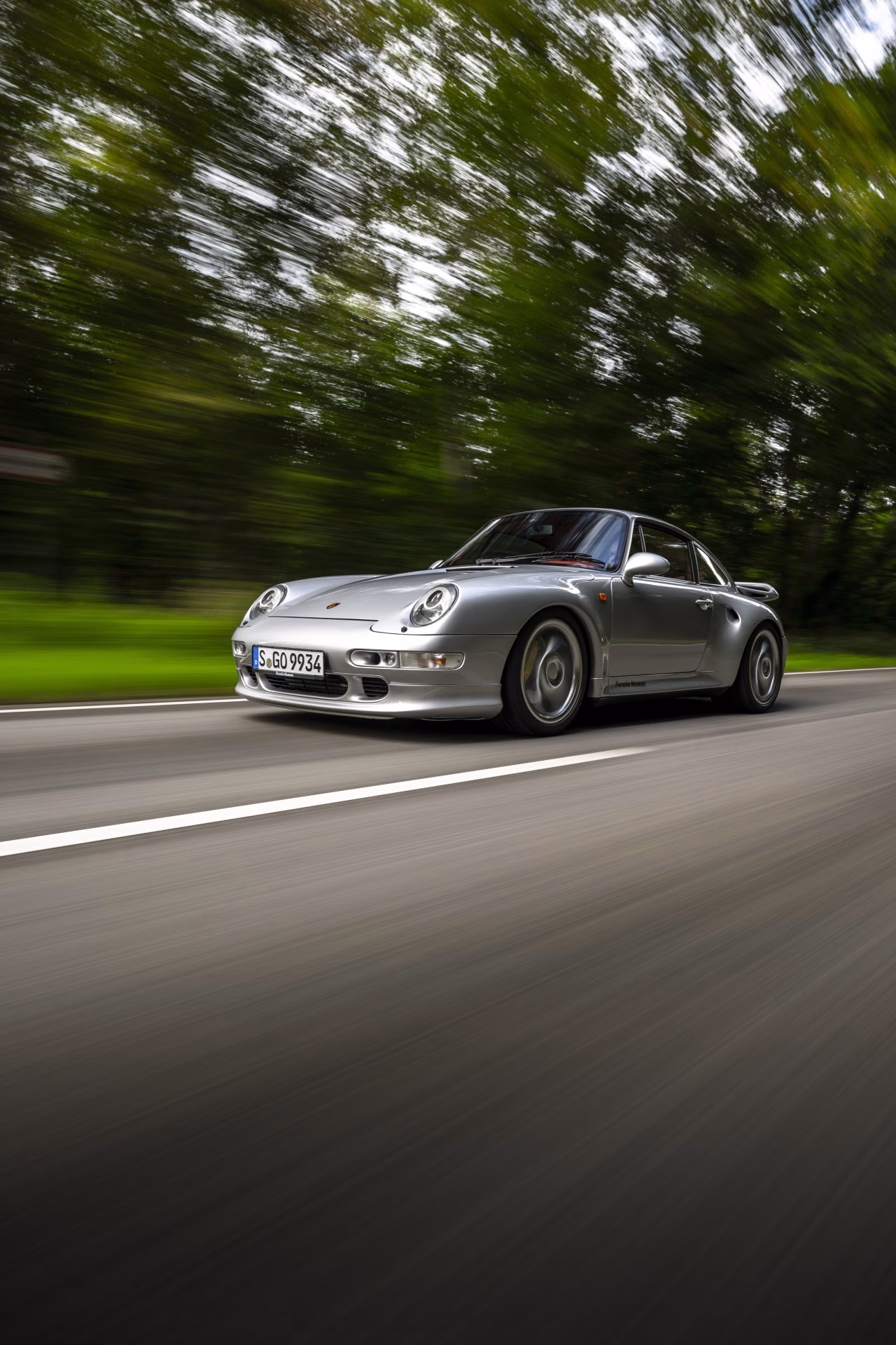 Silver Porsche 911 993 Turbo driving on a tree-lined road