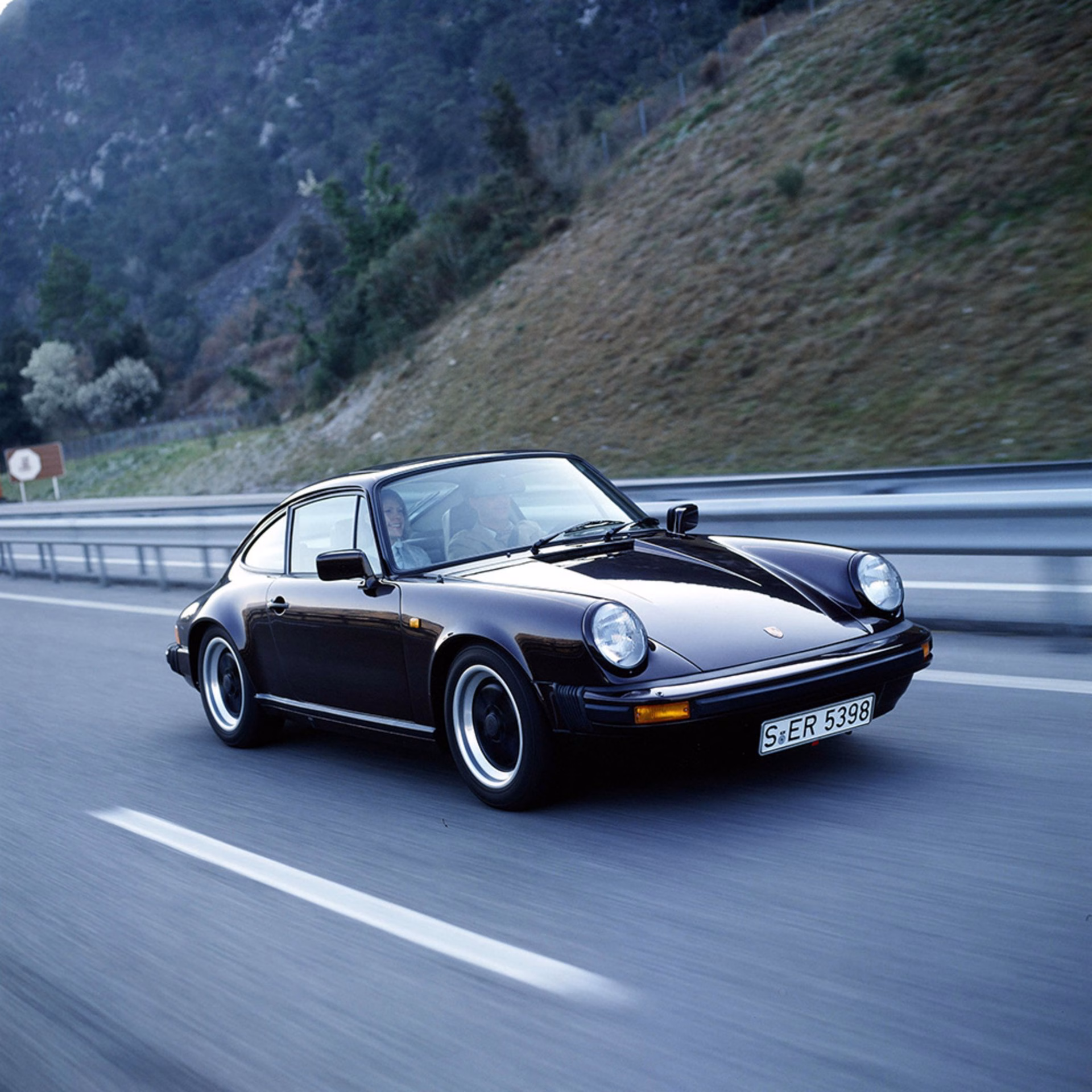Dark brown early Porsche 911 coupe driving on a mountain road